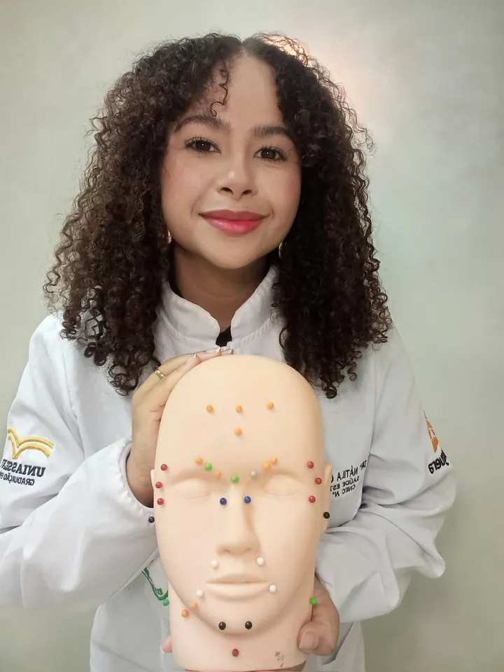 Drª Náth Harmonier segurando um modelo de rosto com os pontos de aplicação da harmonização